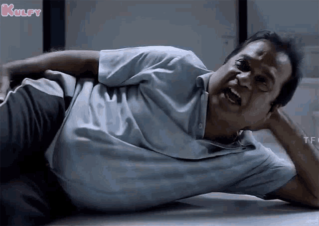 a man is laying on the floor with his mouth open and his hands behind his head .