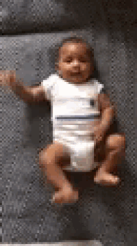a baby in a diaper is laying on a couch waving .
