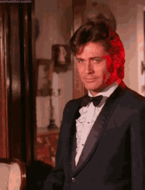 a man in a tuxedo and bow tie stands in a room