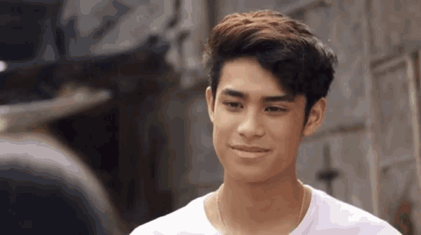a young man wearing a white shirt is smiling and looking at another man .