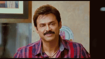 a man with a mustache is wearing a striped shirt and a necklace and making a funny face .