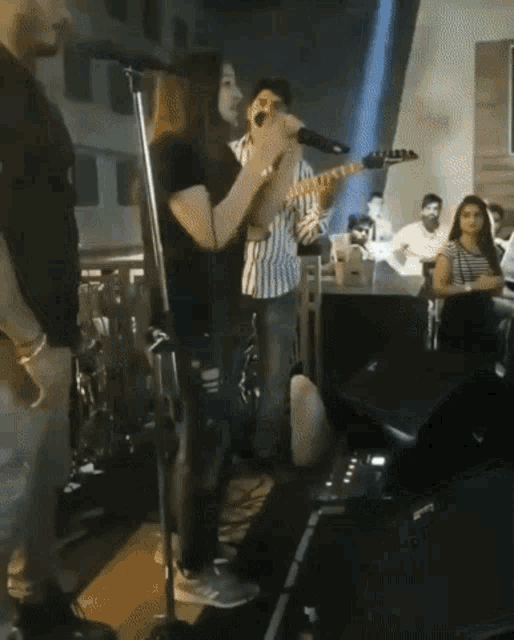 a woman singing into a microphone while a man plays a guitar in front of a crowd