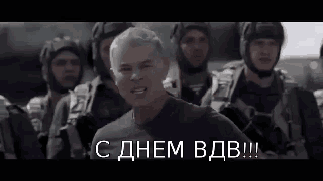 a man in a military uniform is standing in front of a group of soldiers with russian writing on the bottom .