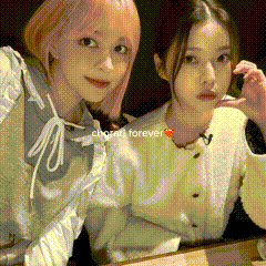 two girls are sitting next to each other and one has pink hair and the other has black hair .