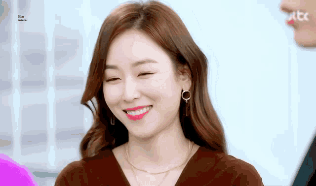 a woman wearing earrings and a necklace is smiling and winking at the camera .