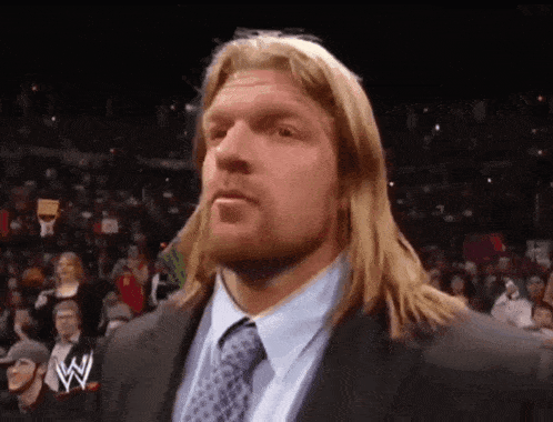 a wrestler in a suit and tie stands in front of a crowd .