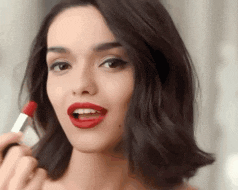 a woman is applying red lipstick on her lips .