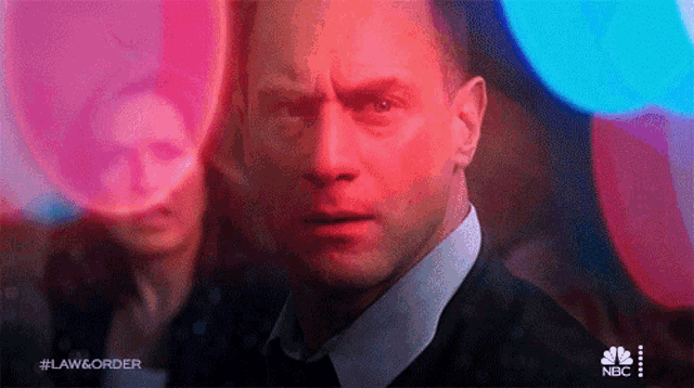 a man in a suit and tie is looking at the camera while a woman stands behind him .