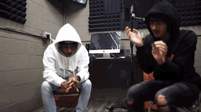 a man in a white hoodie with the word supreme on it sits next to a man in a black hoodie
