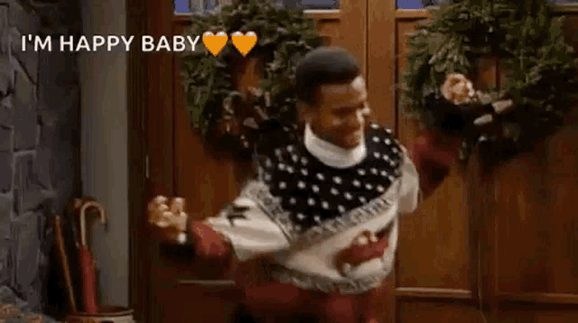 a man in a sweater is dancing in front of a door with a wreath on it .