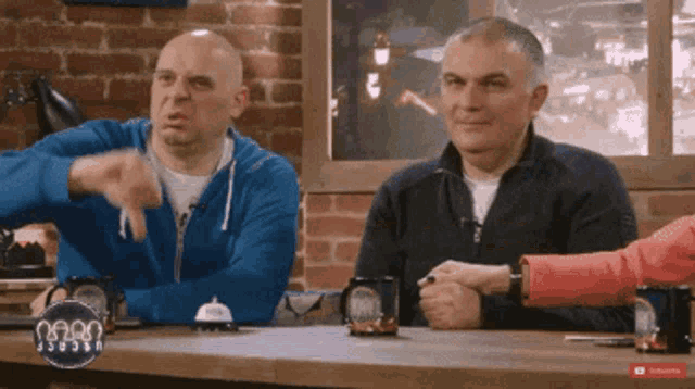 two men sit at a table with a sign that says ' subscribe ' on it