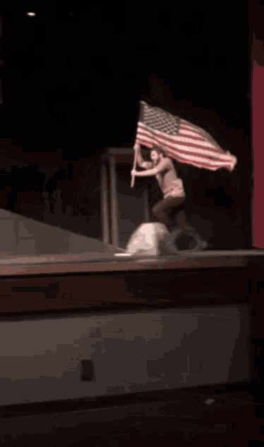 a person holding an american flag on a stage in a dark room