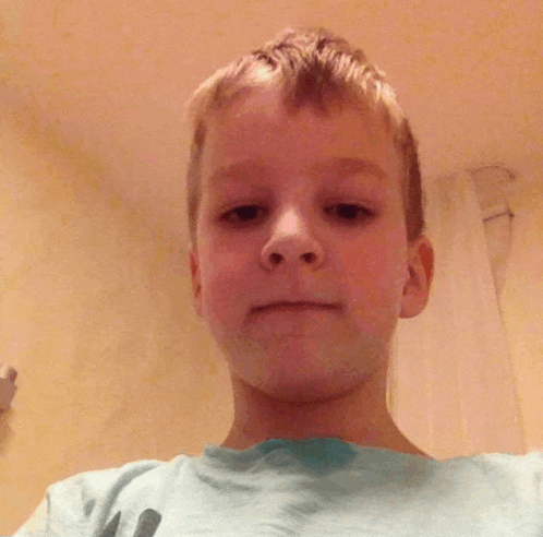 a young boy in a blue shirt looks at the camera with a sad look on his face