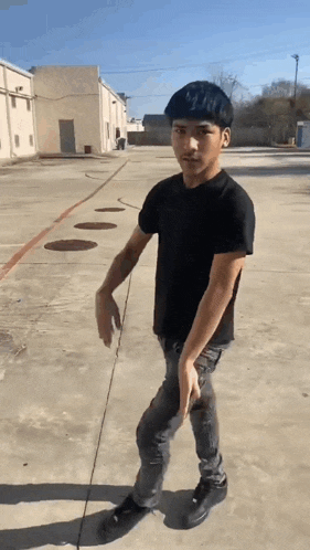 a young man in a black shirt is standing on a concrete sidewalk .