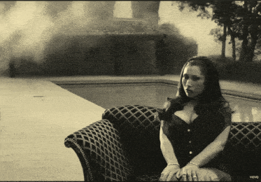a woman in a corset sits on a couch in front of a swimming pool with the word vevo on the bottom