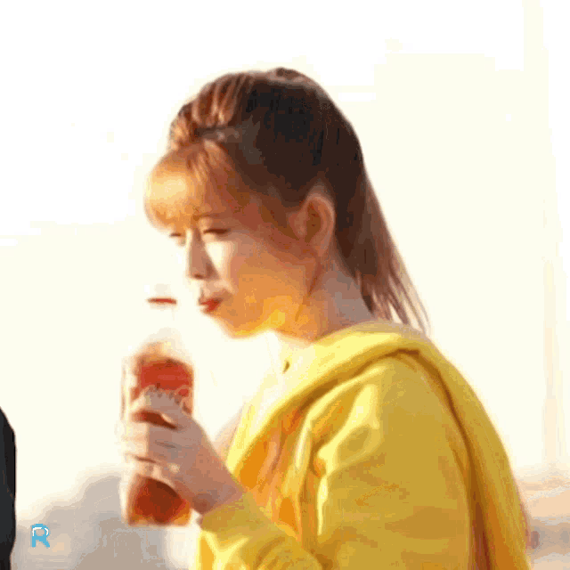 a woman in a yellow jacket drinks from a bottle
