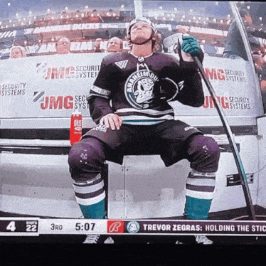 a hockey player is sitting on the bench holding a stick with jmg security systems in the background