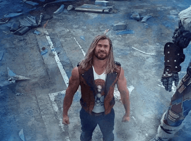 a man with long hair and a beard is standing in front of a robotic arm