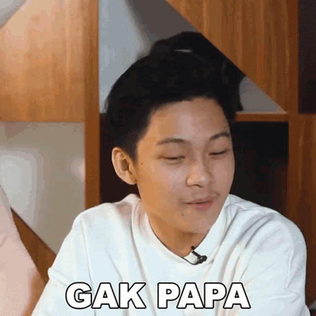 a young man wearing a white shirt is making a funny face and says " cak papa "