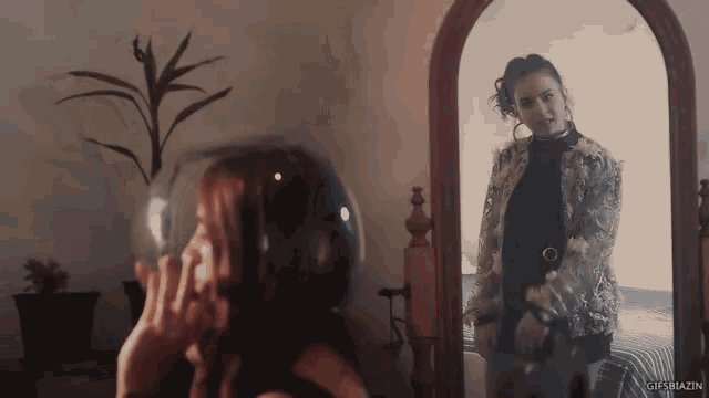 a woman is looking at herself in a mirror with gifsbazin written on the bottom