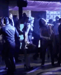 a group of people dancing in a dark room with purple lights