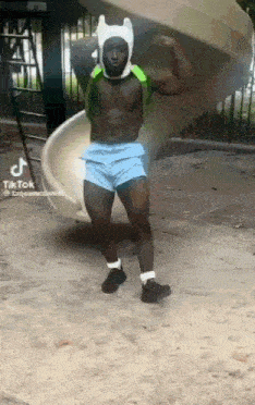 a shirtless man is standing in front of a slide in a park .