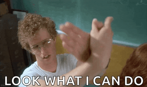 a man with curly hair and glasses is giving a high five to another man in a classroom .