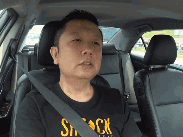 a man in a car wearing a black shirt that says shock on it