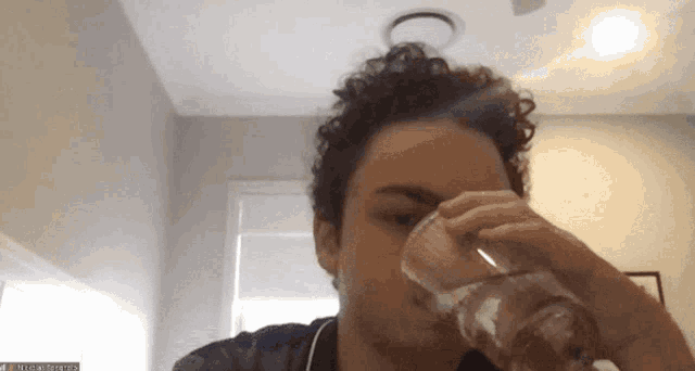 a man is drinking a glass of water in front of a screen that says ' nick ' on it