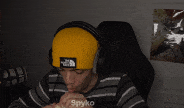 a person wearing headphones and a yellow beanie that says the north face