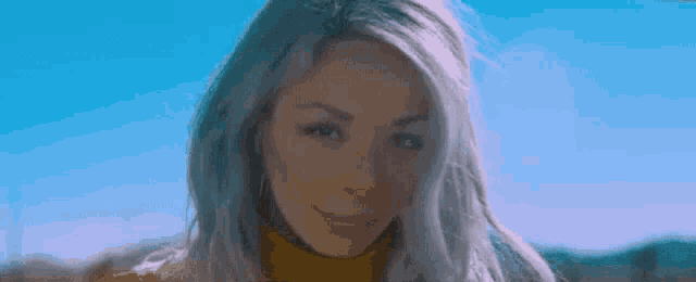 a close up of a woman 's face with a blue sky in the background and a yellow turtleneck .