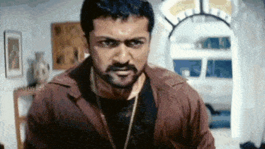 a man with a beard wearing a brown jacket and a black shirt is looking at the camera .