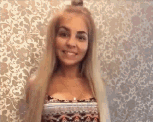 a woman with long blonde hair is smiling and standing in front of a wall .