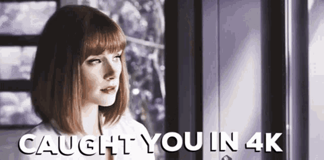 a woman is standing in front of a window with the words caught you in 4k written above her .