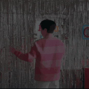 a man in a pink jacket is dancing in front of a tinsel curtain