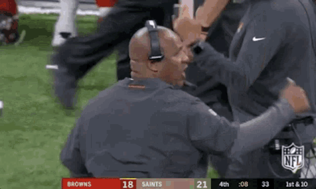a man wearing headphones is talking to another man on a football field