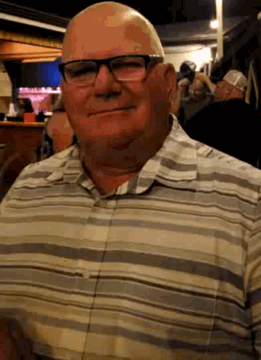a bald man wearing glasses and a striped shirt smiles