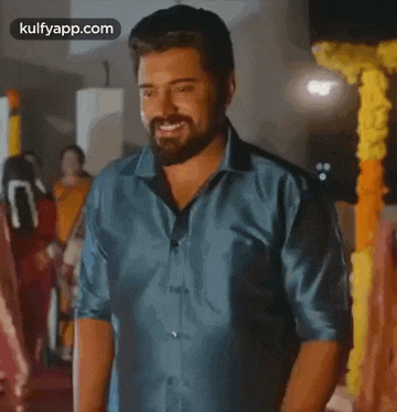 a man with a beard is smiling while standing in front of a flower arrangement .