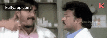 two men are standing next to each other in a room talking to each other .
