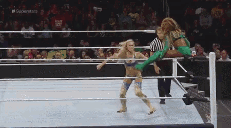 two women are wrestling in a ring with a referee in the background