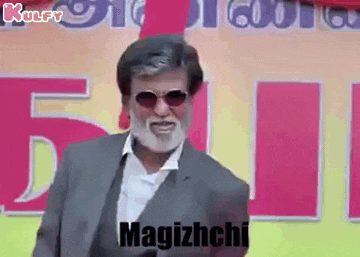 a man with a beard wearing sunglasses and a suit is standing in front of a sign that says magizhchi .