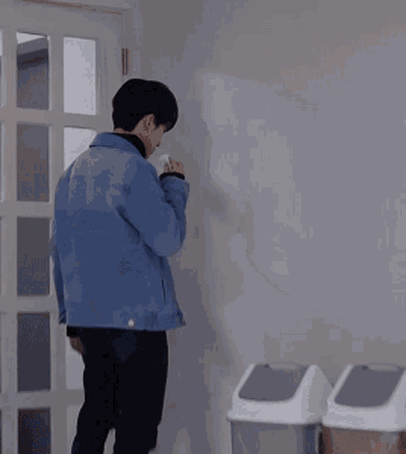 a man in a blue jacket is leaning against a wall holding a cup