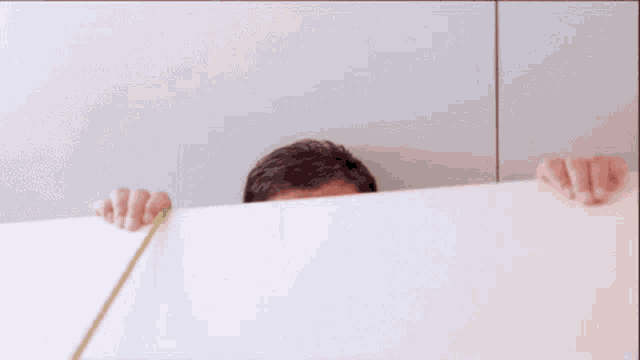 a man is peeking over a white wall holding a white sign