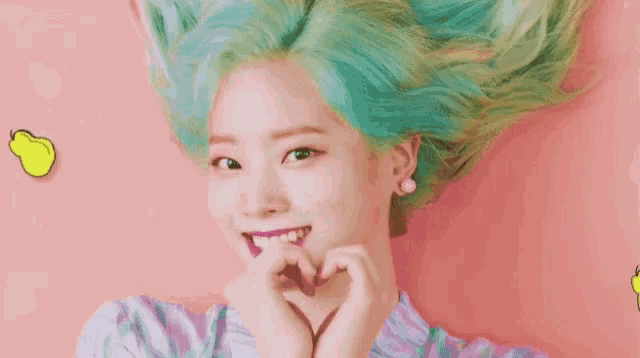 a girl with green hair is making a heart shape with her hands