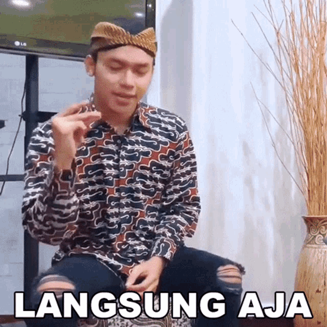 a man wearing a hat and a shirt is sitting in front of an lg tv and says langsung aja
