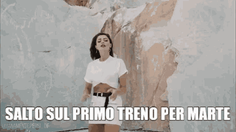 a woman in a white dress is standing in front of a wall with the words salto sul primo treno per marte above her .