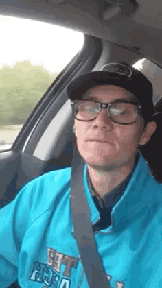 a man wearing glasses and a hat is sitting in a car with a seat belt .