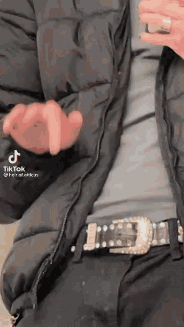 a person wearing a black jacket and a black belt with a rhinestone buckle .