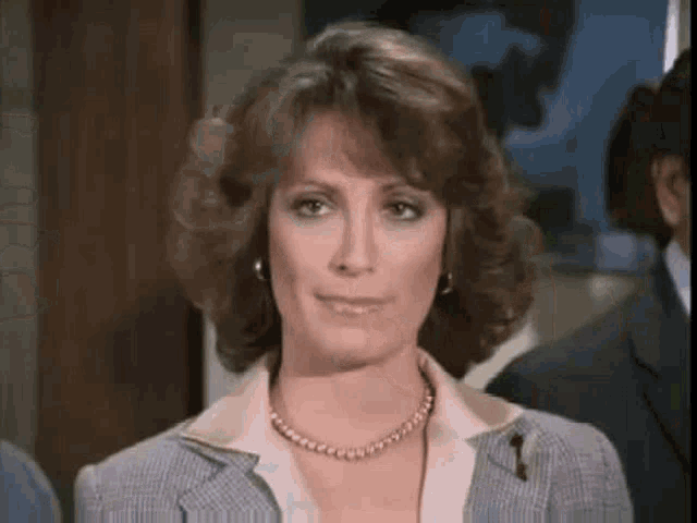 a woman in a suit and pearl necklace is looking at the camera and smiling .