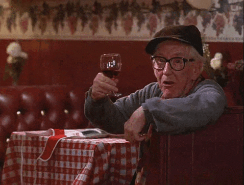 a man with glasses and a hat is holding a glass of wine